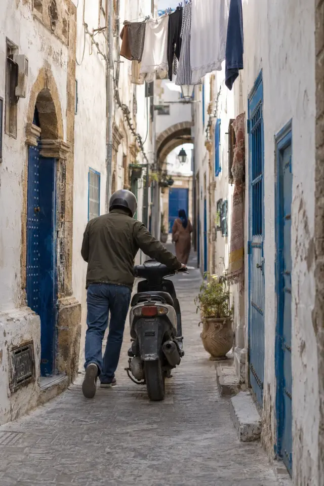 Un scooter poussé à la main dans une ruelle blanche et bleue