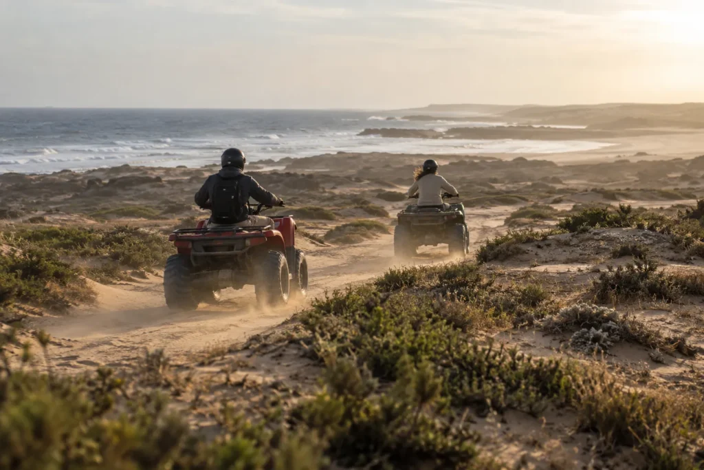 Deux quads sur une piste de sable entre les dunes, l'océan à l'horizon